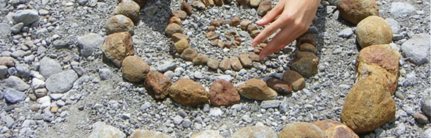 Χέρια που υφαίνουν μια σπείρα από πέτρες για τις βιωματικές τελετές μυθικής σύνδεσης της Haqãt.